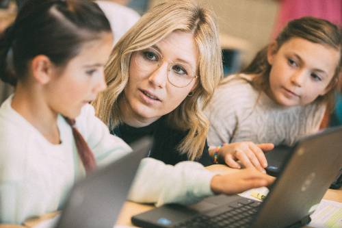 Adult working with 2 children on laptops