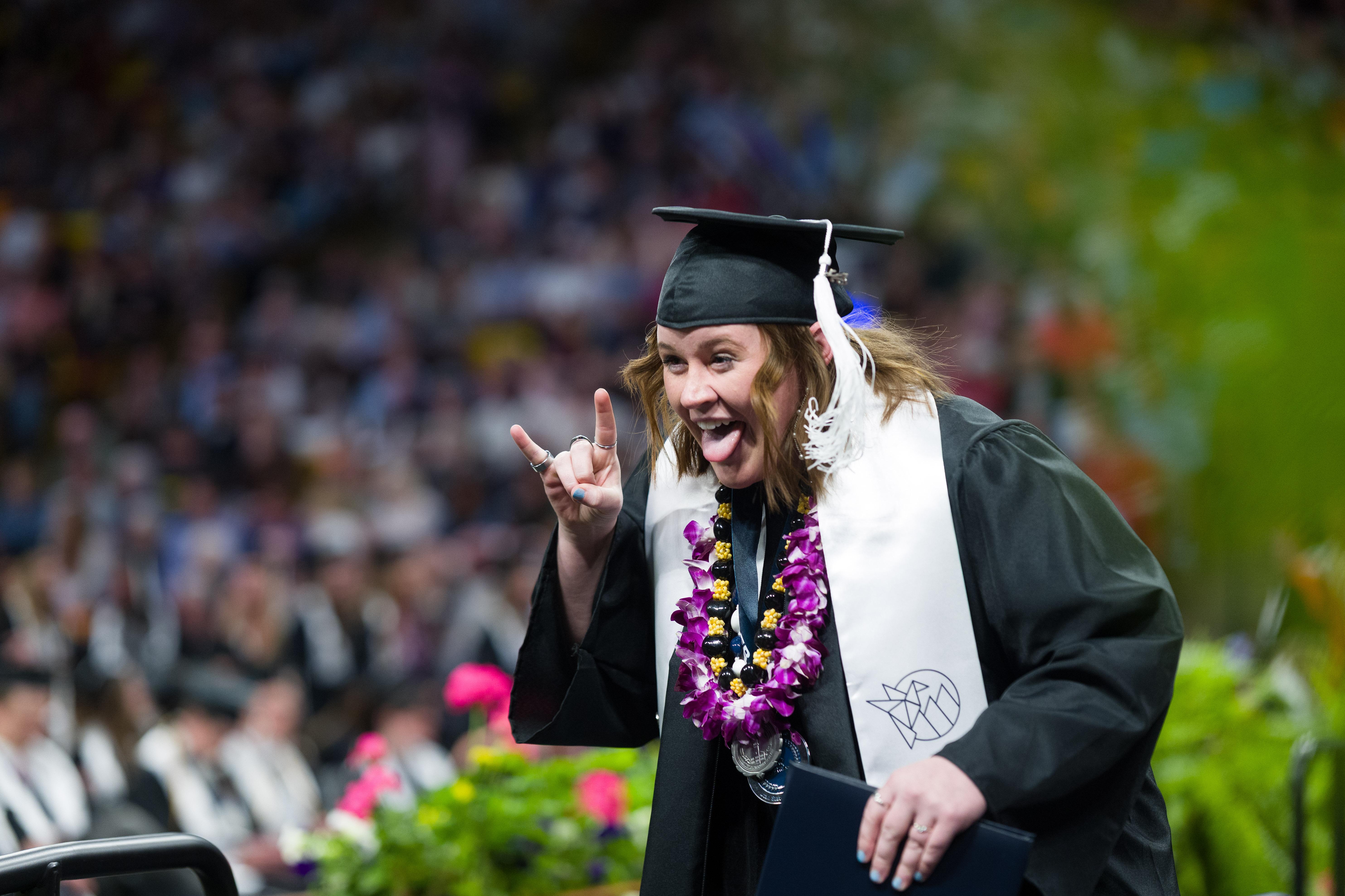 graduate throwing bull horns with their hand, with their tongue out