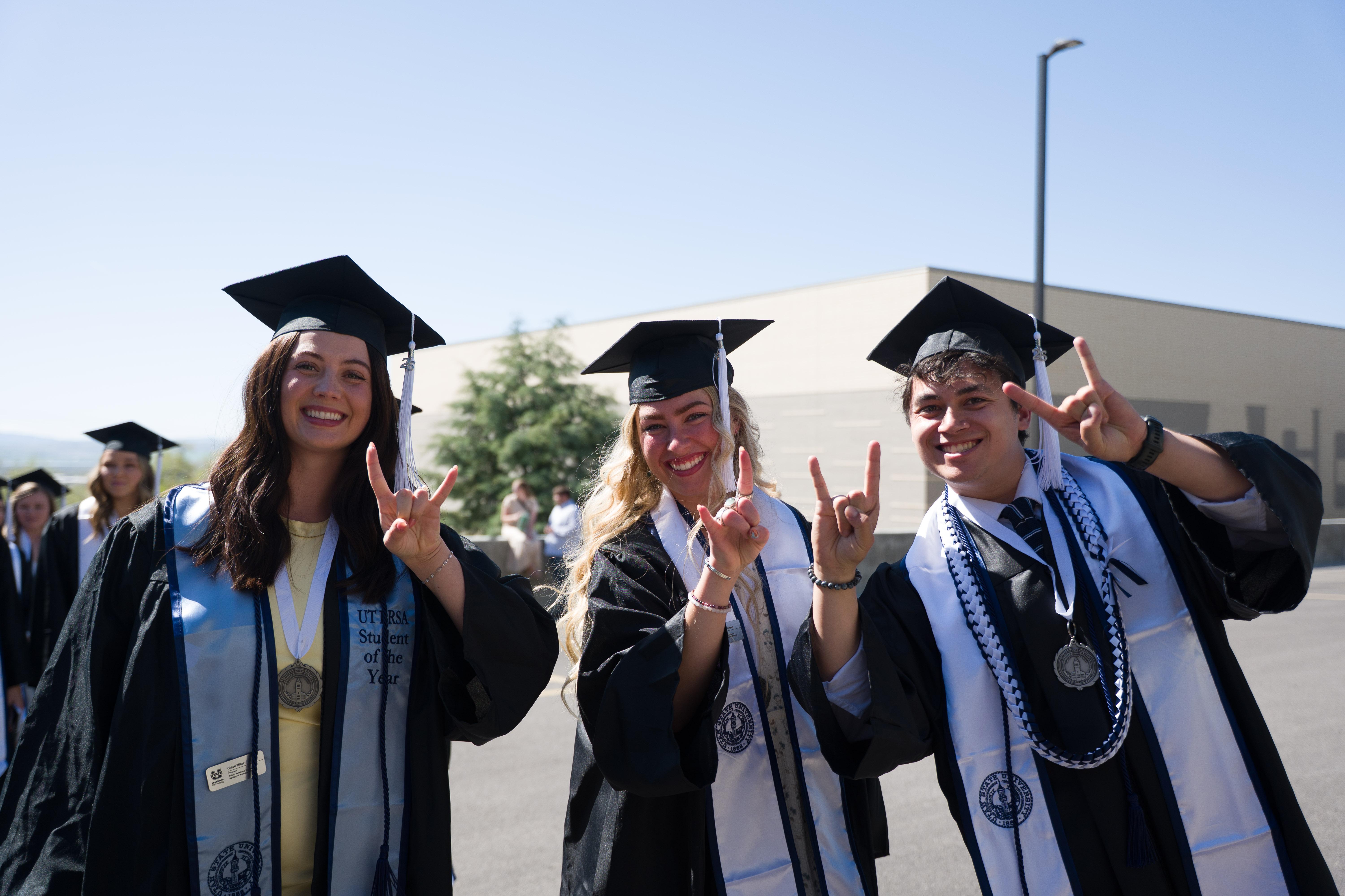 a group of graduates throwing up bull horns with their hands after the ceremony