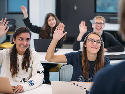 Students in a classroom raising their hand.