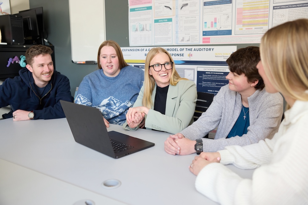 Professor and four students sitting at a table having a discussion.